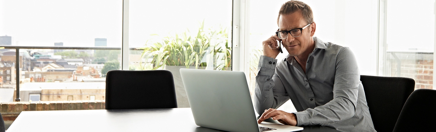 Professional man in glasses working on a laptop while talking on the phone, to help illustrate services procurement and Statement of Work (SoW) solutions.