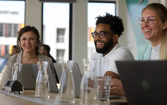 Three professionals collaborating at a meeting table with laptops, representing Hays employer branding and talent engagement services.