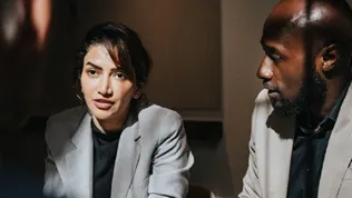 Two professionals seated in discussion in a formal indoor setting, illustrating senior‑level engagement within a public‑sector environment.